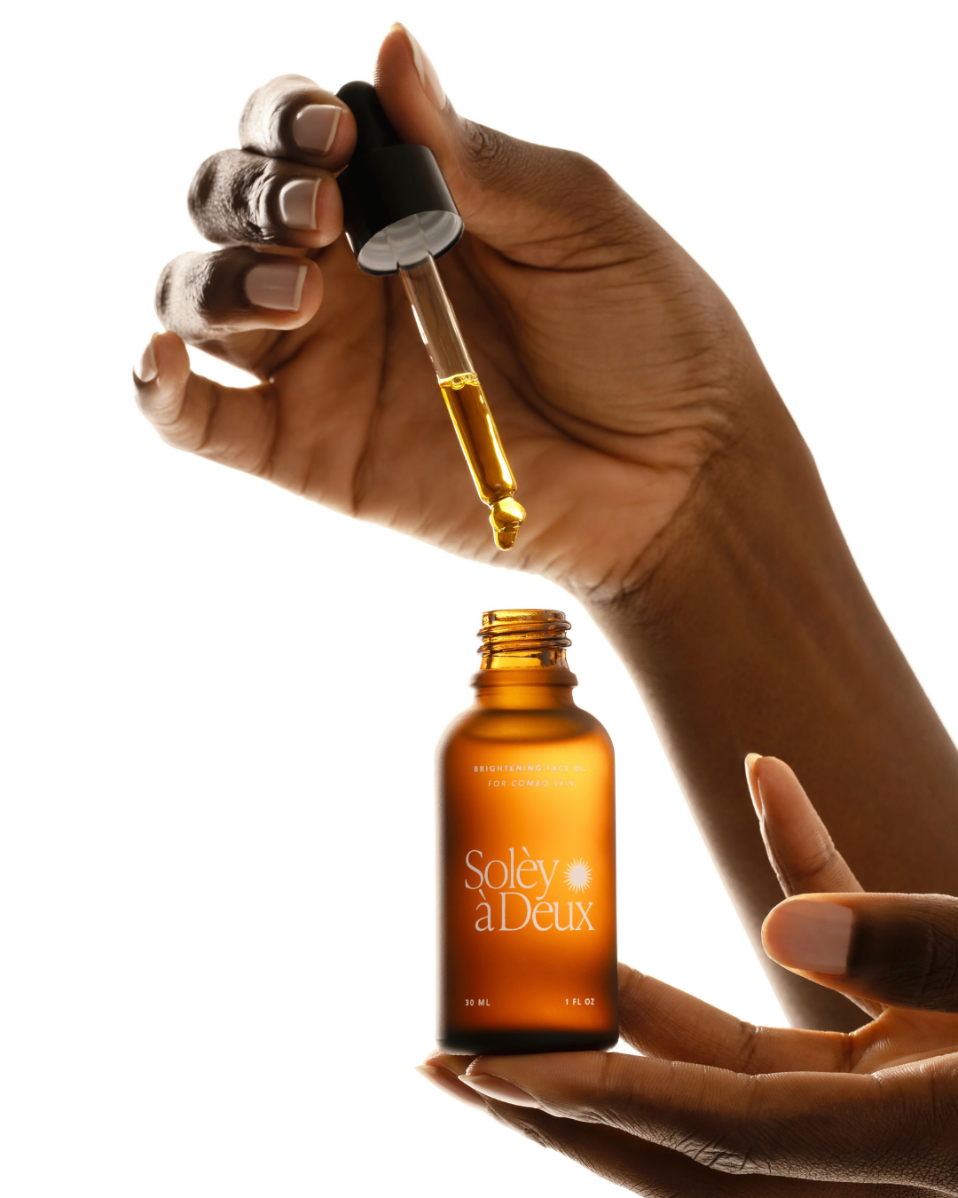 Hand lifting a dropper from Brightening Face Oil for combo skin